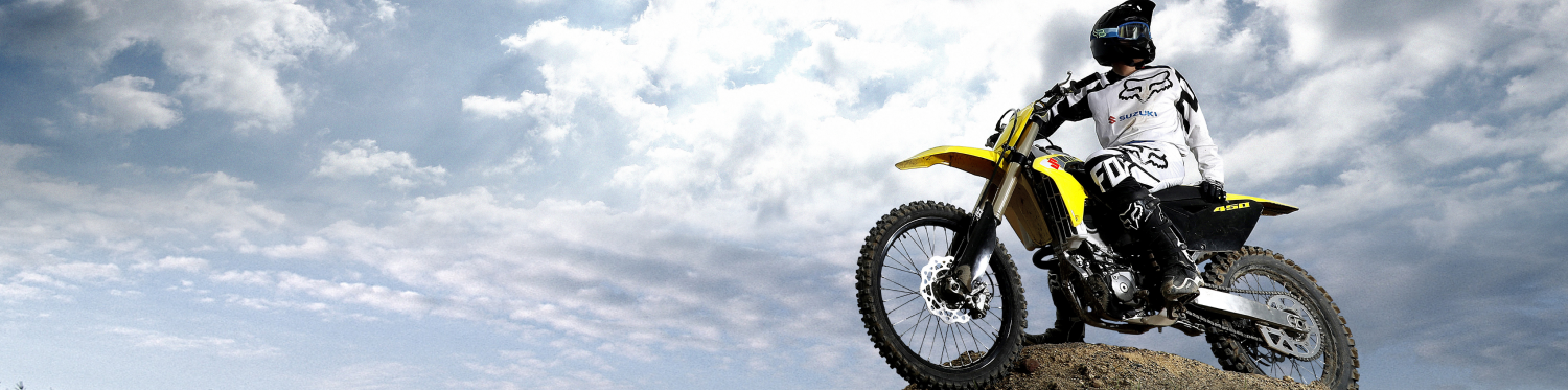 Person on a dirt bike parked on top of a hill under partly cloudy skies